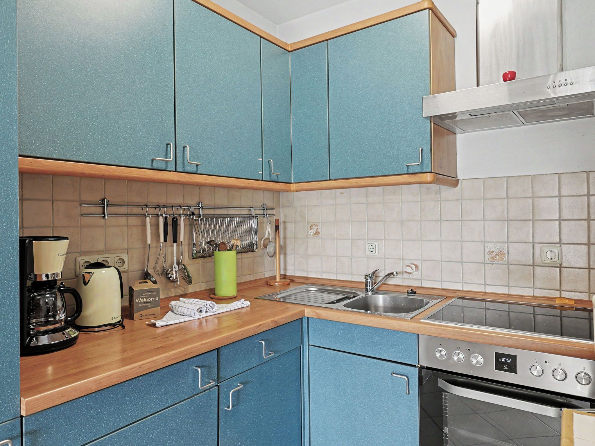 A kitchen with blue cabinets, a coffee maker, a kettle, a sink, and an oven.