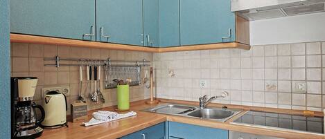 A kitchen with blue cabinets, a coffee maker, a kettle, a sink, and an oven.