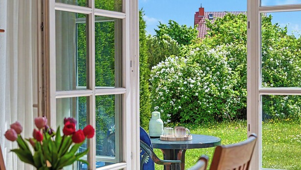 A table with a vase of flowers, a chair, and a view of a garden through a window. - Achterwasser App. 13 by Interhome (Zempin)