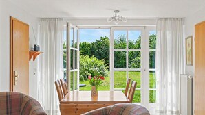 A dining area with a table, chairs, a plaid sofa, a vase with flowers, and a view through large glass doors to a garden. - Achterwasser App. 13 by Interhome (Zempin)
