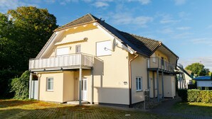 En toetagers bygning med balkon i stueetagen, en lille tilhørende garage og en belagt indkørsel.