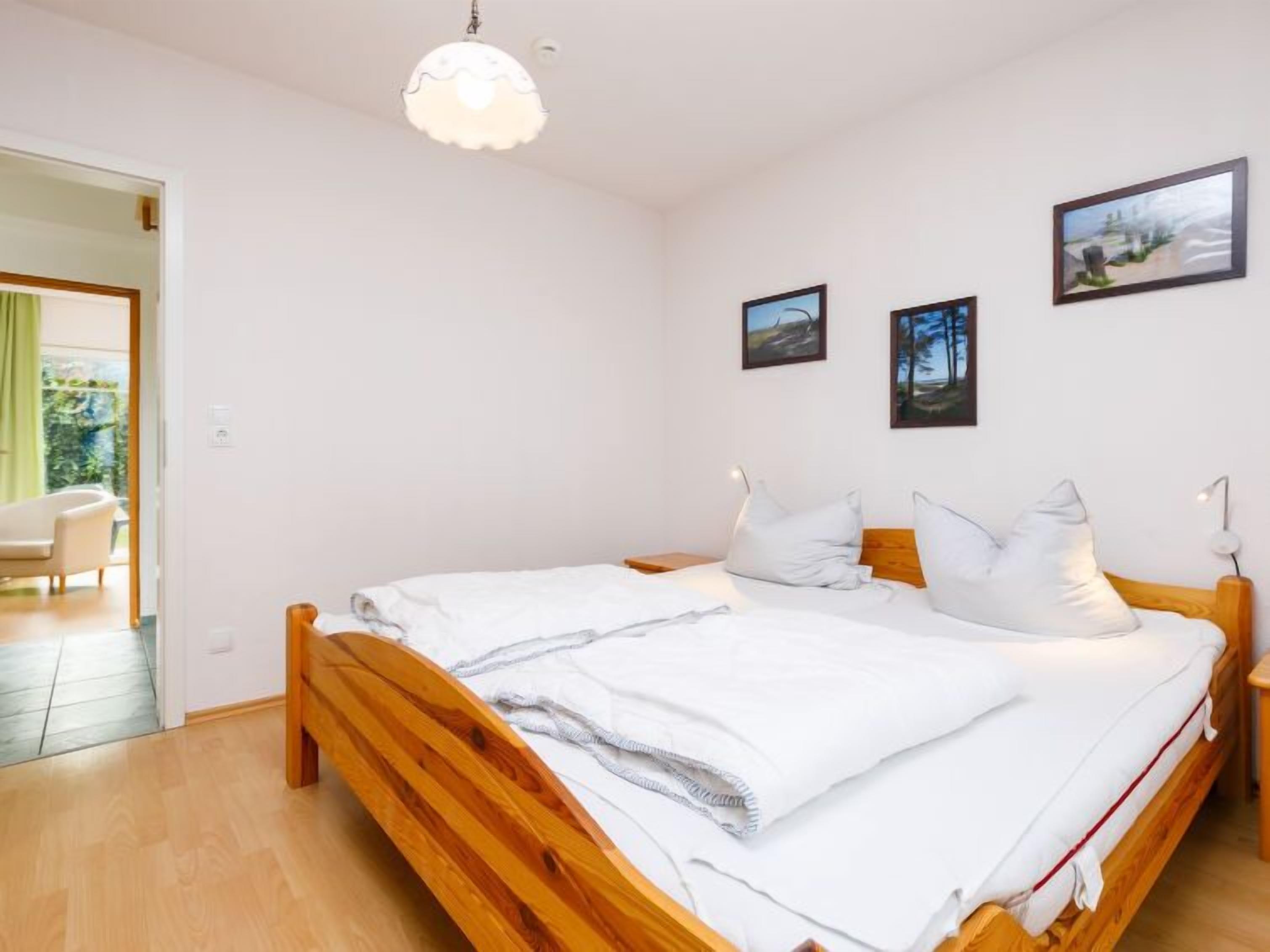 Ein Schlafzimmer mit einem hölzernen Bett, weißer Bettwäsche und zwei gerahmten Bildern an der Wand.