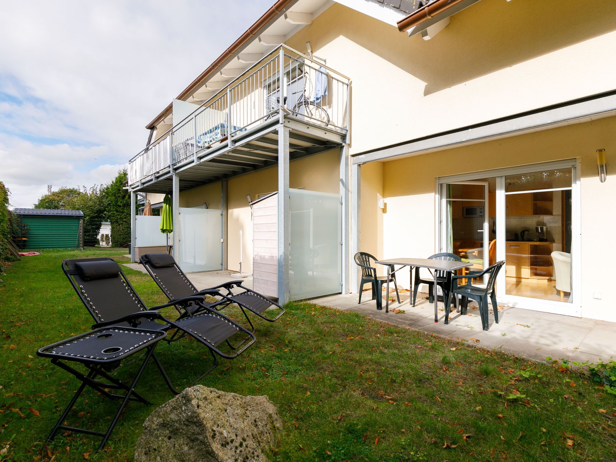 Ein Wohnhaus mit Balkon, einer Terrasse mit Liegestühlen, einem Essbereich und einer Garage.
