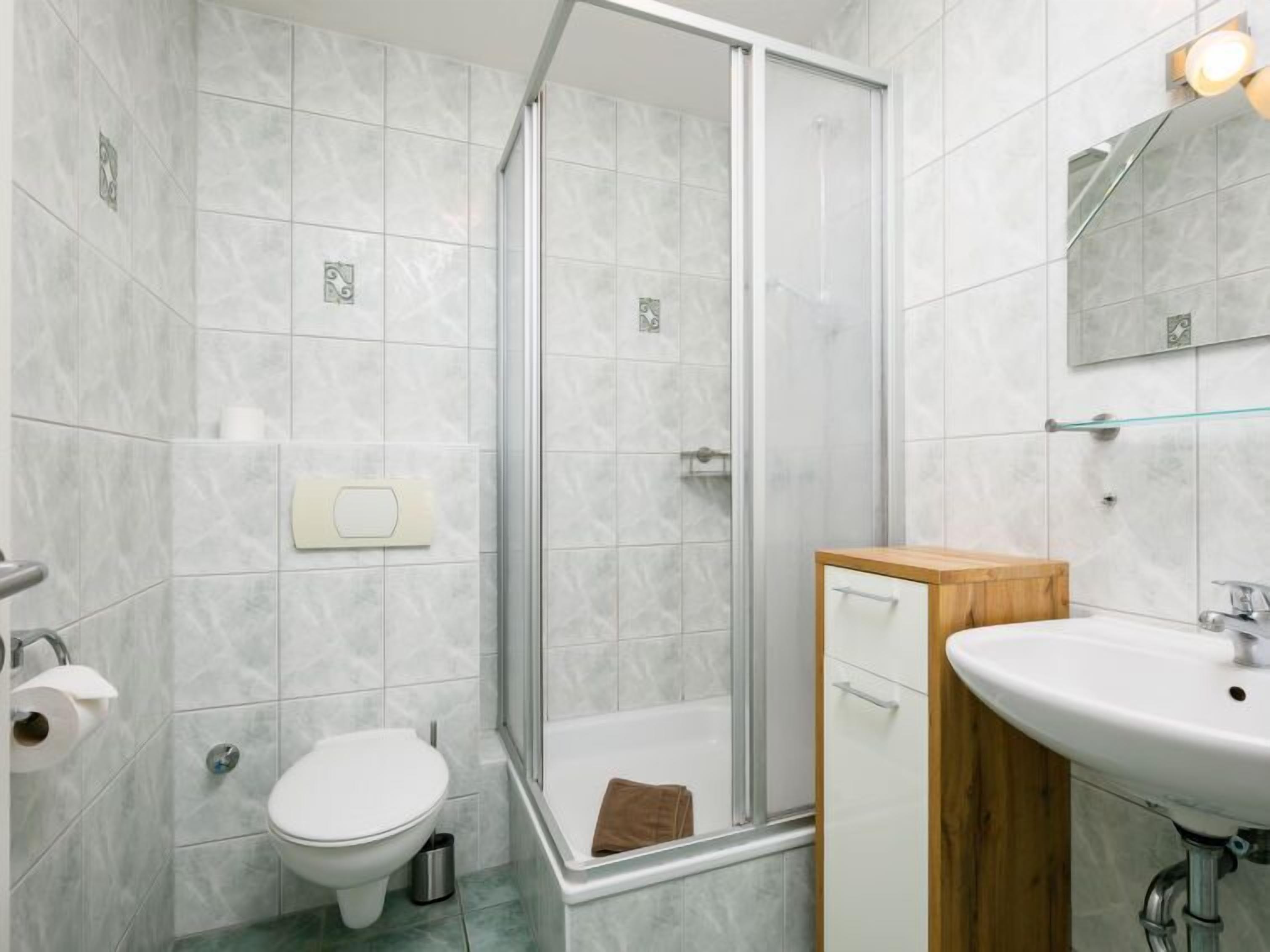 Um banheiro moderno com box de vidro, vaso sanitário, pia e armário de madeira.