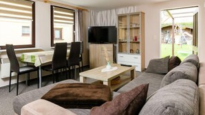 A modern living room with a sofa, a coffee table, a TV, and a dining area with chairs and a table. - Vacation home Ehmke by Interhome (Karlshagen)