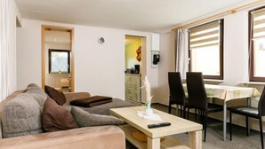 A modern living room with a sofa, a dining table with chairs, a small table with a vase and remote control, and a kitchen area in the background. - Vacation home Ehmke by Interhome (Karlshagen)