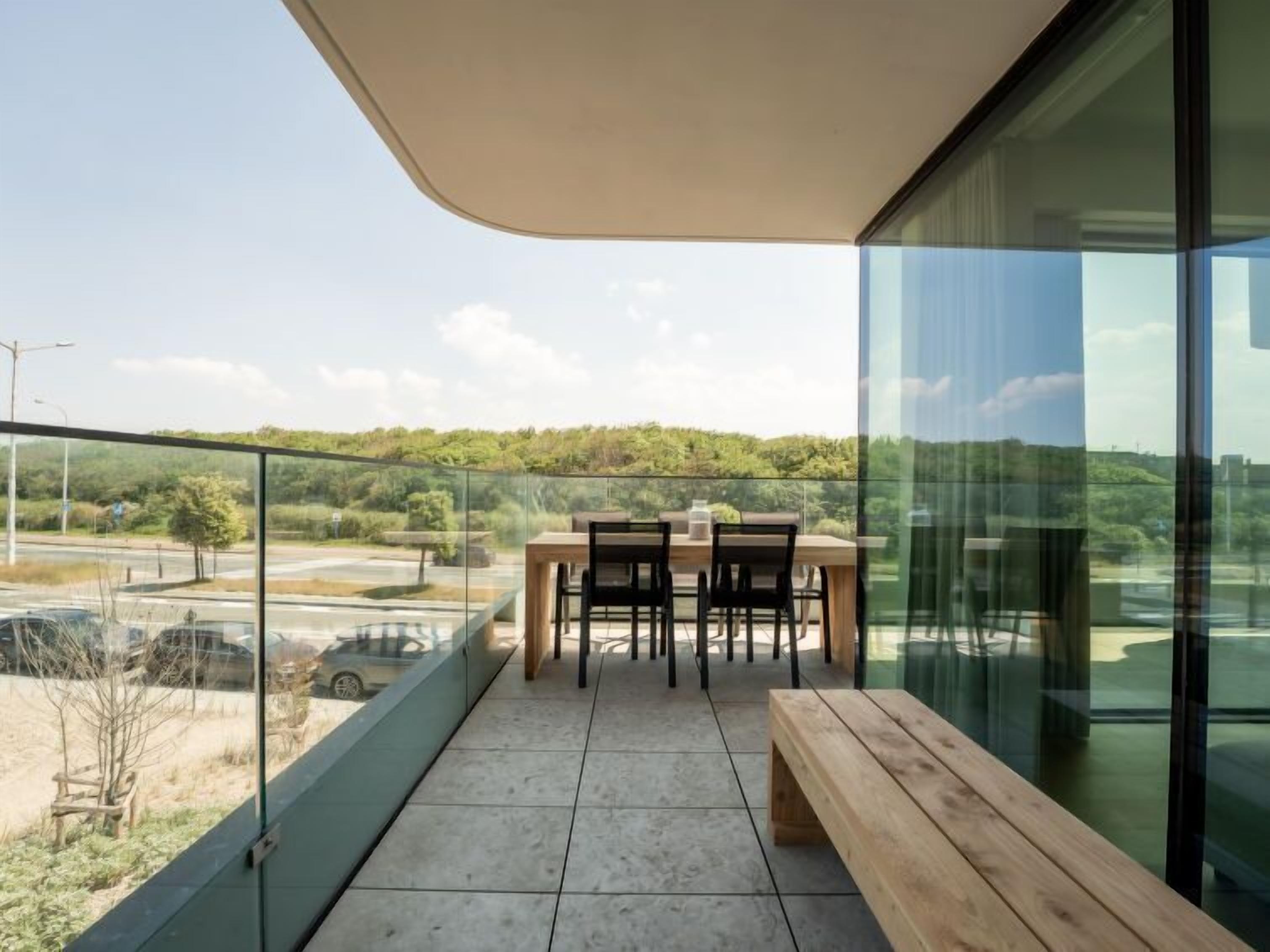 A balcony with a table and chairs, a wooden bench, and a glass railing.