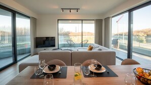 A modern living room with a sofa, dining table set with glasses and plates, and a TV on the wall. - One with terrace and dune view by Interhome (Blankenberge)