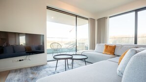 A modern living room with a flat-screen TV, a grey sofa, a small round table, and a balcony with a glass railing. - One with terrace and dune view by Interhome (Blankenberge)