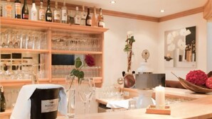 Un coin bar avec des étagères remplies de bouteilles et de verres, un seau portant l’inscription « HOCHE », et une bougie posée sur le comptoir.