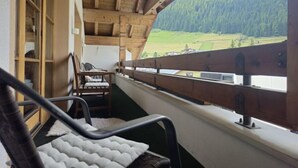Un balcon doté d’une balustrade en bois, d’un banc rembourré et offrant une vue sur un paysage montagneux.