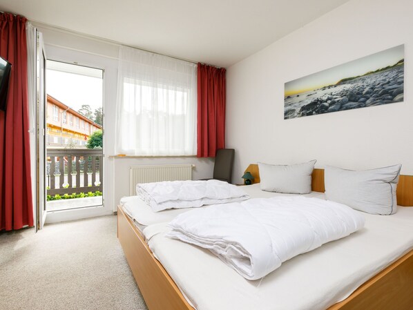 A hotel room with a bed, a window with curtains, a radiator, a painting on the wall, and a view of the outside.