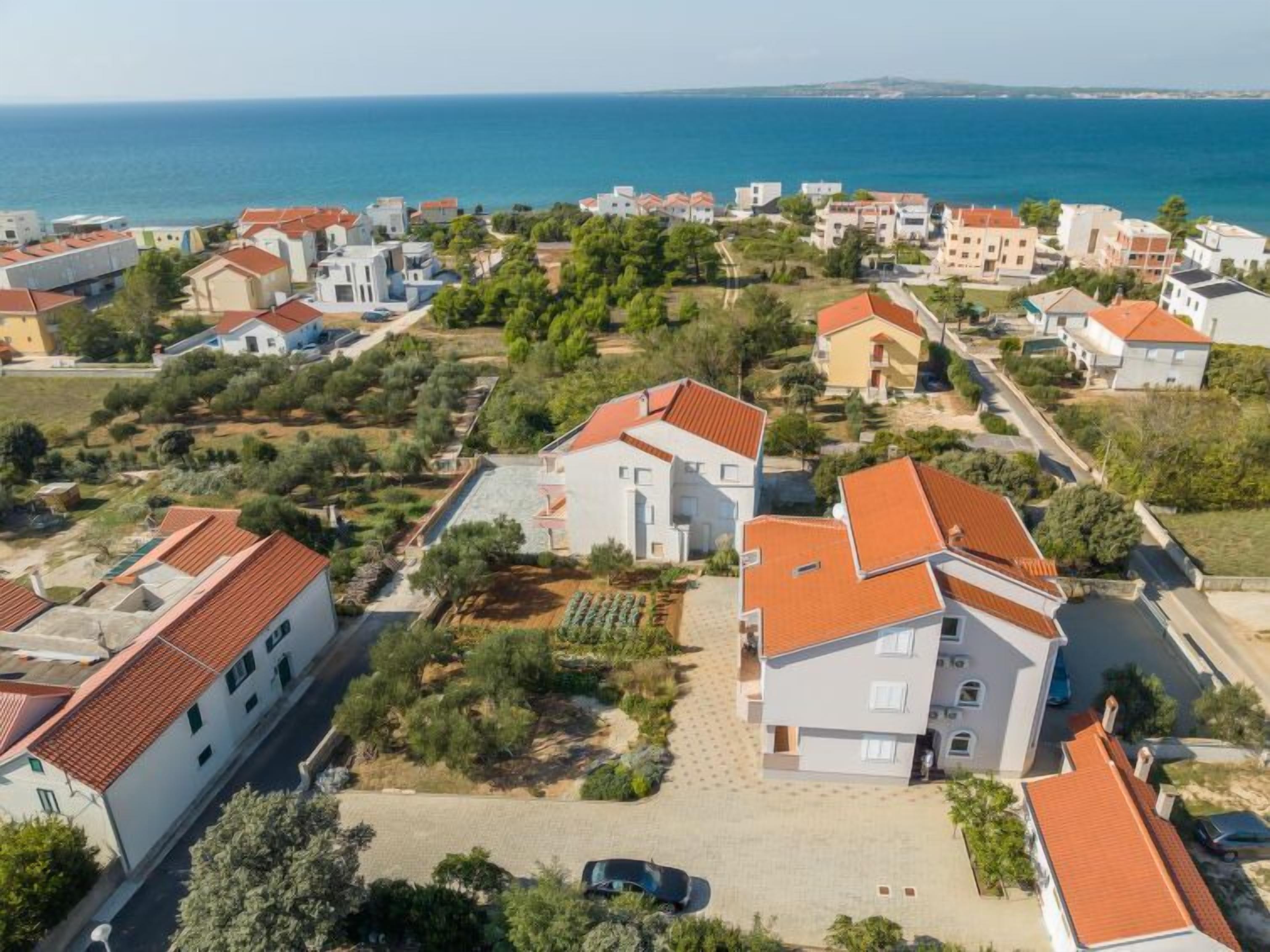 Una zona residencial costera con casas de paredes blancas y techos de tejas rojas, rodeada de vegetación y con una vista despejada al mar.