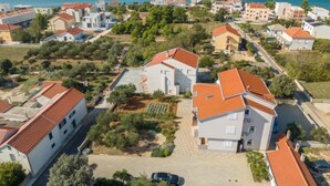 A coastal residential area with houses featuring red-tiled roofs and white walls, surrounded by greenery and a clear view of the sea. - Apartment Irena by Interhome (Privlaka)