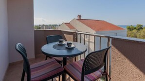 A balcony with a round table and two chairs, overlooking a red-tiled roof and distant buildings. - Apartment Irena by Interhome (Privlaka)