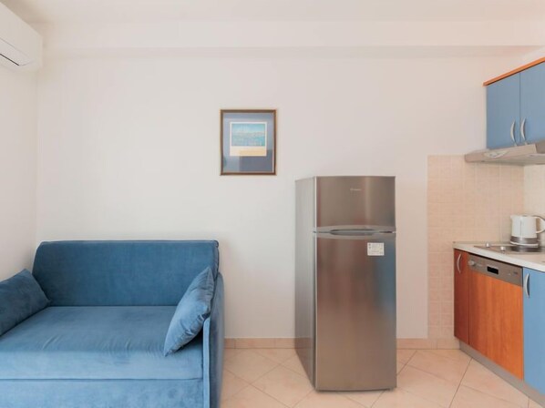 Een compact keukenhoekje met een roestvrijstalen koelkast, een blauwe bank en een lijst met een afbeelding aan de muur.