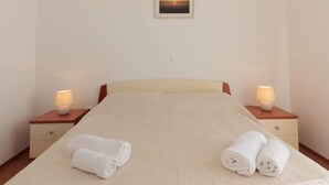 A neatly made bed with two rolled towels, a framed picture on the wall, and bedside lamps on wooden nightstands. - Apartment Irena by Interhome (Privlaka)