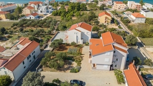 A coastal residential area with houses featuring red-tiled roofs and white walls, surrounded by greenery and a clear view of the sea. - Apartment Irena by Interhome (Privlaka)
