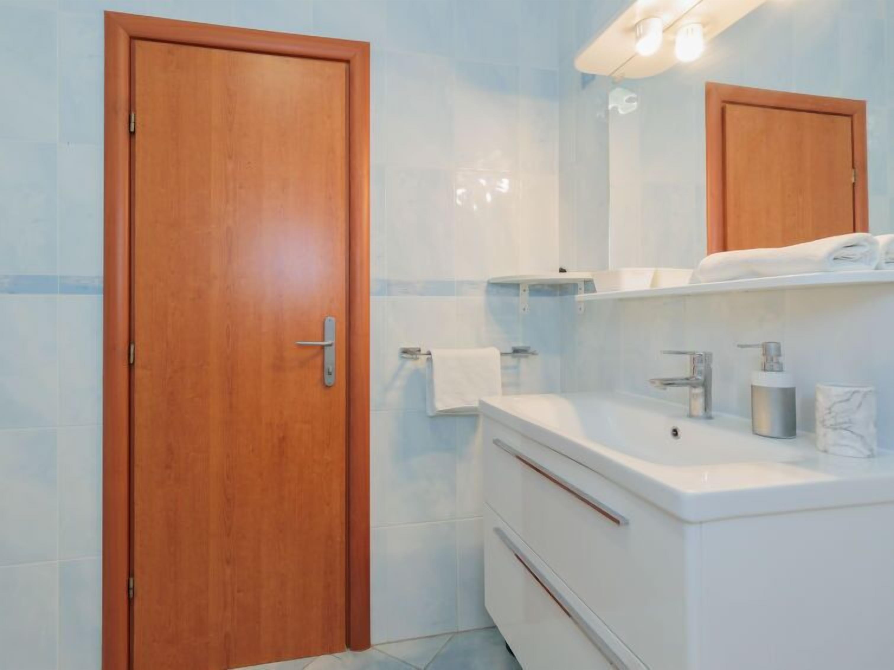 A bathroom with a wooden door, white sink, and a mirror above it.
