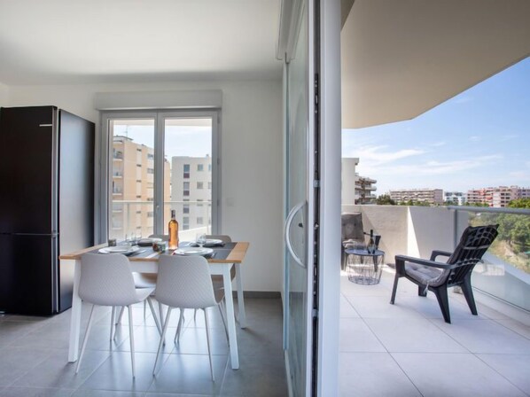 A modern apartment with a balcony, a dining area with a table and chairs, and a view of the cityscape.