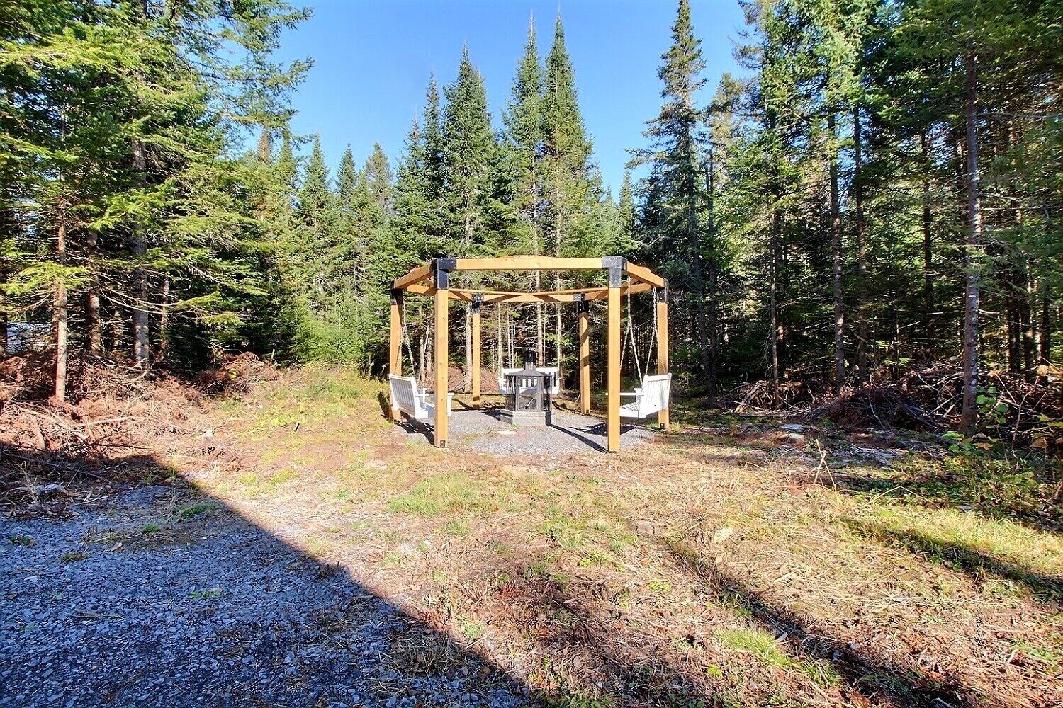 A wooden swing set in a forested area with a gravel path leading to it.