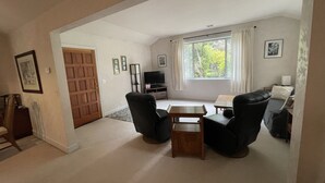 Un salon avec un canapé, des fauteuils, une table basse, un téléviseur et une fenêtre avec des rideaux.