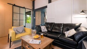 Un soggiorno moderno con una poltrona gialla, un divano in pelle nera e un tavolino in legno con un giornale e un bicchiere di birra.