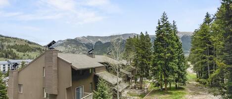 A two-story building with a balcony, surrounded by trees and a mountain view.