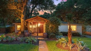 Una casa acogedora y bien iluminada con porche, rodeada de abundante vegetación y un jardín cuidado.