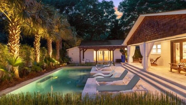 Un área de piscina con sillas de descanso y una zona de estar cubierta.