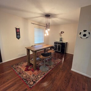 A dining area with a wooden table and chairs, a patterned rug, a ceiling fan, a window with blinds, and a wall decoration. - Cozy 3bdrm 2bath house for families w/ small kids & infants near White Rock Lake (Dallas)