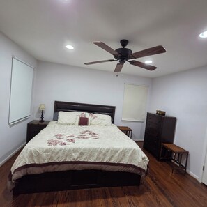 Une chambre à coucher comprenant un lit, un ventilateur de plafond, une table de chevet, une commode et une fenêtre.