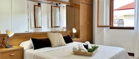 Un dormitorio ordenado con cama, lámparas de noche, armario de madera y ventana con cortinas.