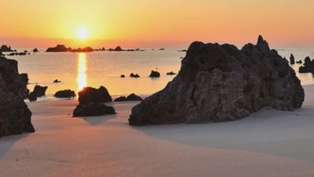 Ein Strand mit großen Felsen und einem Sonnenuntergang.