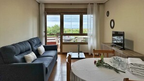 Ein Wohnzimmer mit Sofa, Esstisch, Fernseher und Balkon mit Blick.