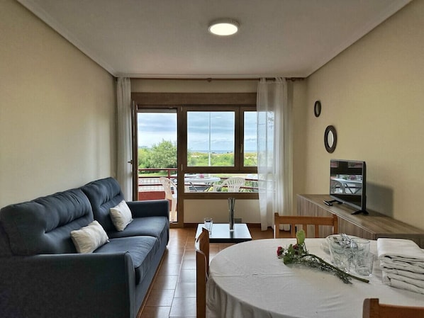 A living room with a sofa, a dining table, a TV, and a balcony with a view.