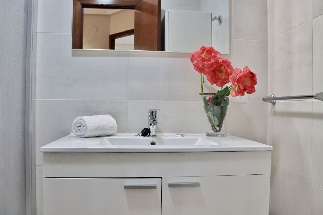 A bathroom with a white sink, a towel, and a vase with flowers.