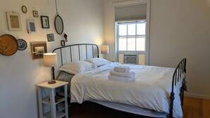 A neatly made bed with white linens, a bedside table with a lamp, and a window with blinds. - Trailside Inn (Mount Stewart)