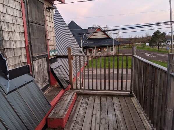 Eine Holzterrasse mit einem Metallzaun, ein kleines Gebäude mit rotem Dach und eine grüne Rasenfläche im Hintergrund.