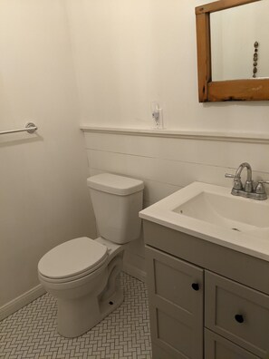 Ein Badezimmer mit Toilette, Waschbecken mit Spiegel darüber und Fliesenboden.