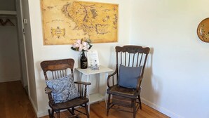 A room with two wooden rocking chairs, a small white table with a map and a vase of flowers, and a wooden floor. - Trailside Inn (Mount Stewart)