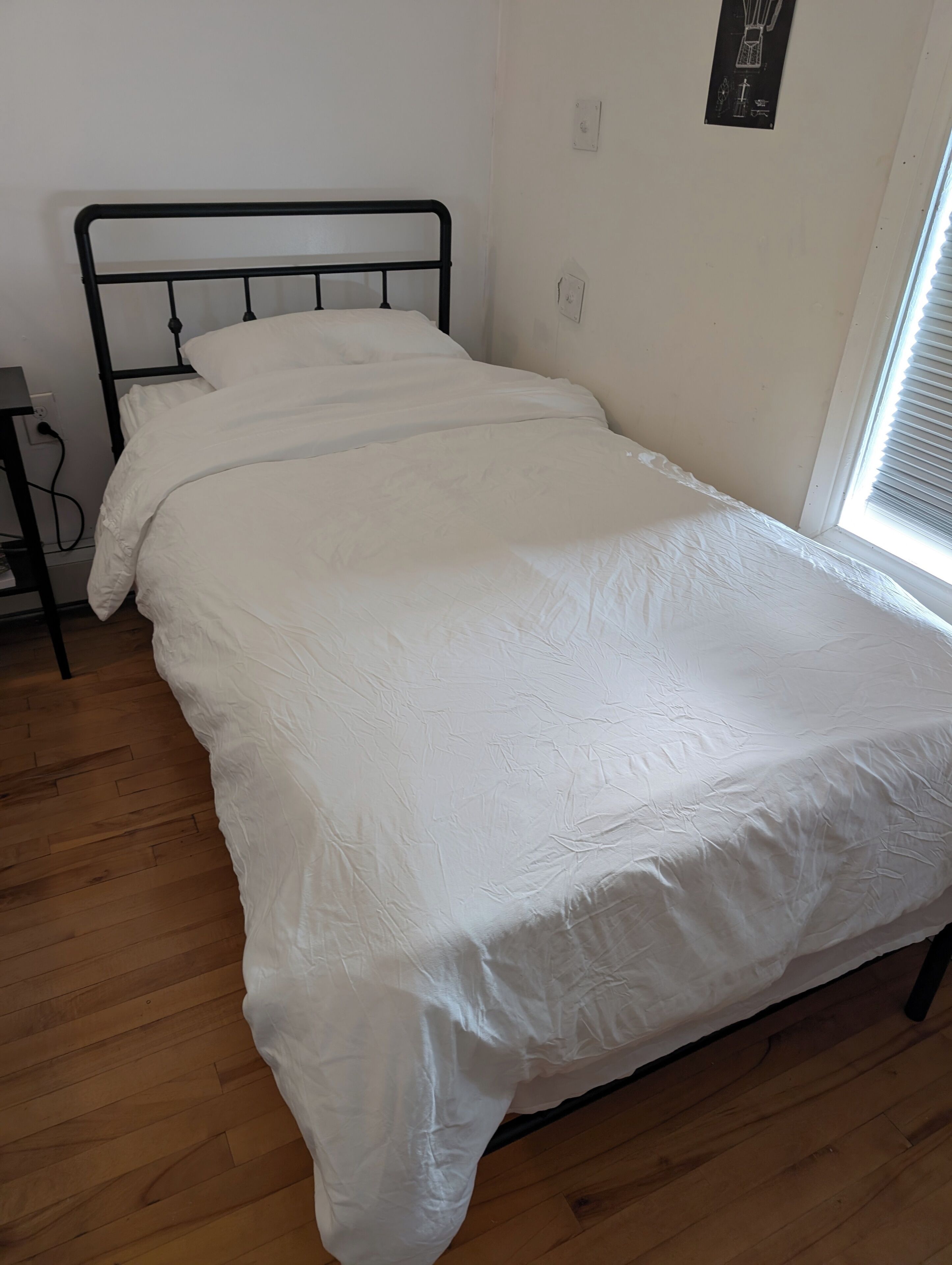 A single bed with a metal frame, white bedding, and a wooden floor.