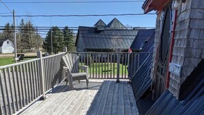 A wooden deck with a metal railing, a single Adirondack chair, and a house with solar panels. - Trailside Inn (Mount Stewart)