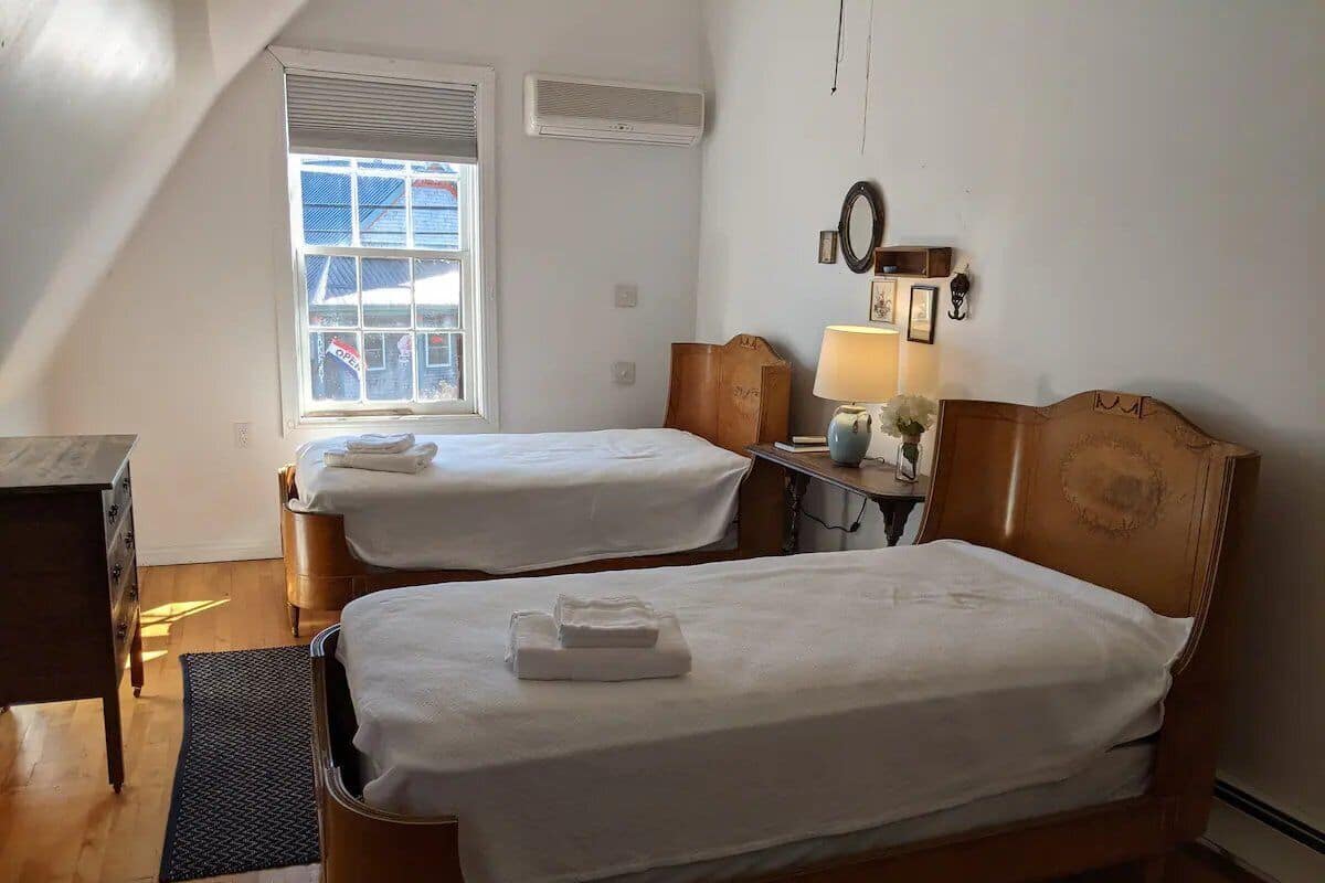 A room with two wooden beds, a desk, a window, and a wall-mounted air conditioner.
