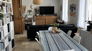 A modern living room with a dining area, a bookshelf, a TV, and a painting. - A 5 du Centre et des Plages, Maison Avec Jacuzzi (Sanary-sur-Mer)