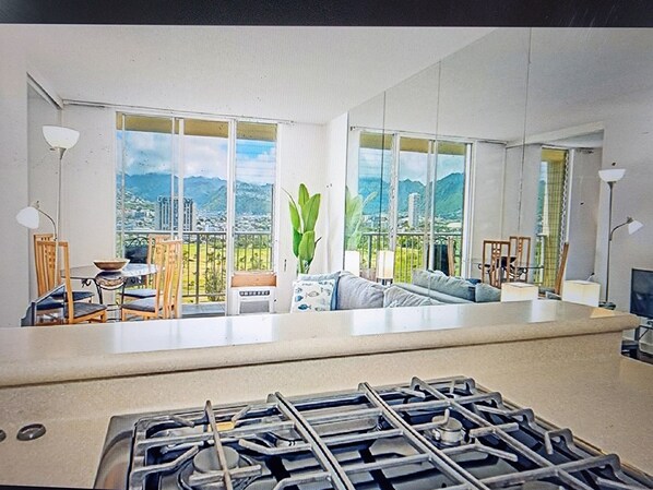 A modern kitchen with a gas stove, large windows offering a view of mountains and greenery, and a dining area with chairs and a table.