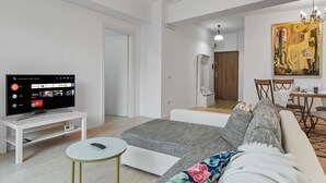 A modern living room with a flat-screen TV on a white stand, a grey sofa, a small round table, and a colorful blanket. - 1BDR Apartment close to Unirii Square (Bucharest)
