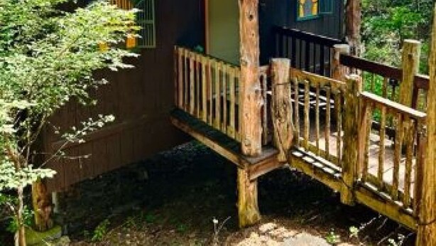 A rustic wooden cabin with a porch and a small deck, surrounded by trees. - Chateau Treehouse #11/ Oak Crest (Eureka Springs)