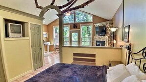 A bedroom with a bed, a TV, a fireplace, and a view of the outdoors. - Chateau Treehouse #11/ Oak Crest (Eureka Springs)