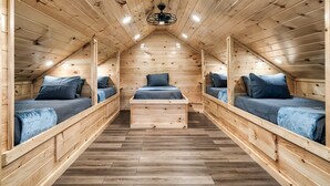 Camera mansardata in legno con due letti a castello, un letto centrale e una ventola a soffitto.